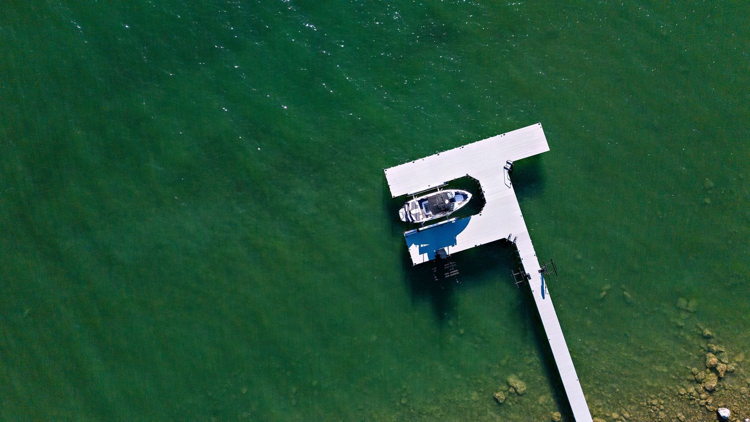 Aerial view of a T-shaped dock extending into bright turquoise waters surrounded by lush green vegetation.