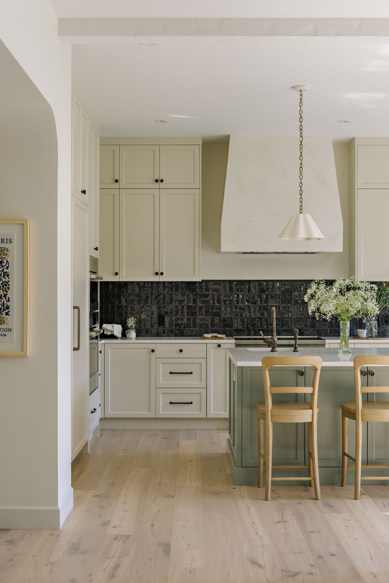 Open concept kitchen with light wood floors, cream cabinets and pendant lighting showcases modern design.