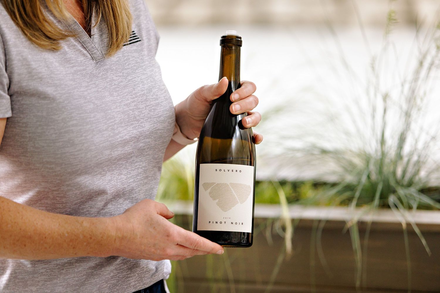 Someone holding a bottle of wine displaying the label against a bright outdoor background.