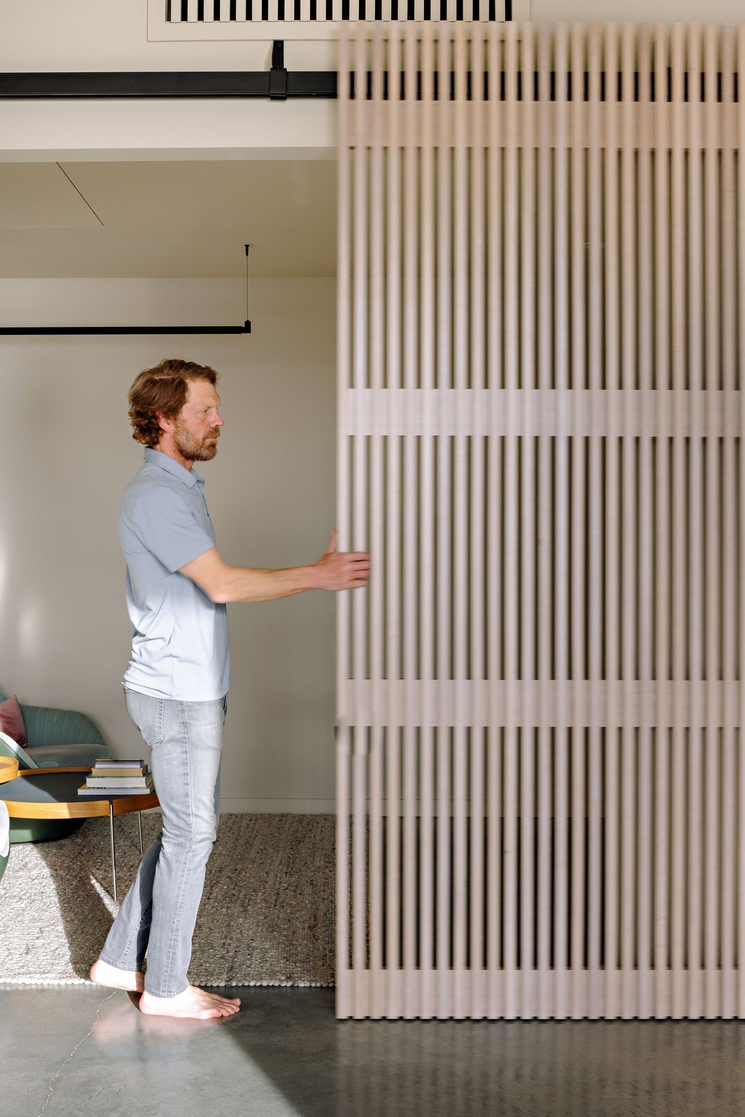 Person in light blue shirt and white pants opens a modern slatted wall panel in minimalist interior space.