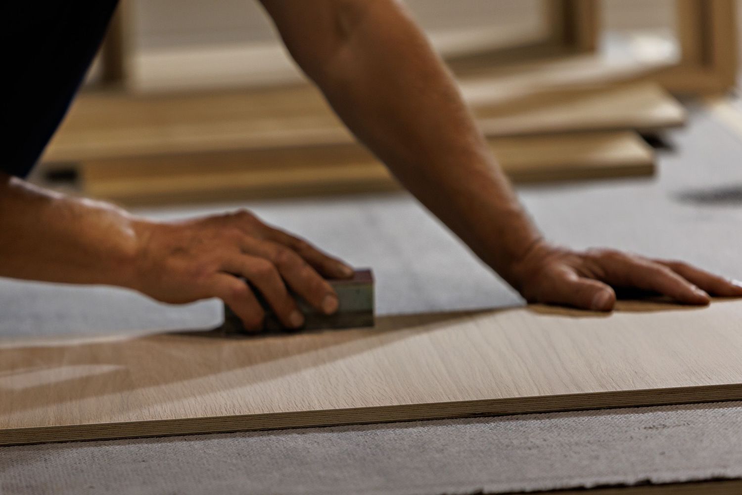 Close-up view of hands installing light wood laminate flooring panels in a home renovation project.