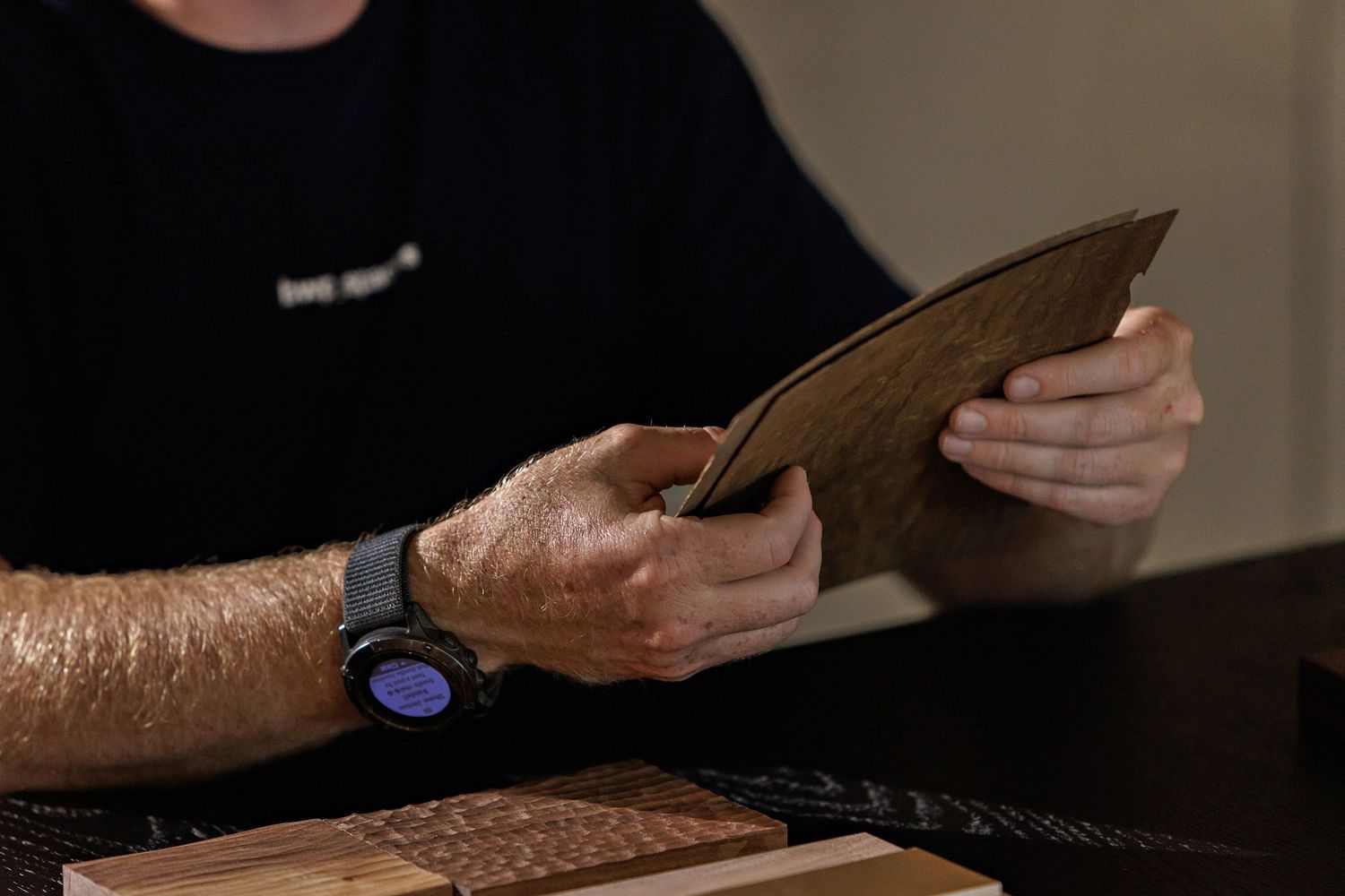 Close-up view of hands holding a leather wallet while wearing a smart watch with dark background.