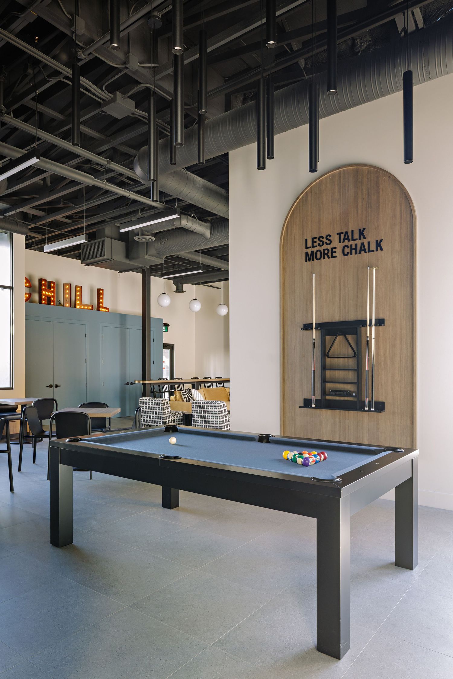 Modern game room interior with pool table and wall text reading 'Less Talk More Chalk' under an arched alcove.