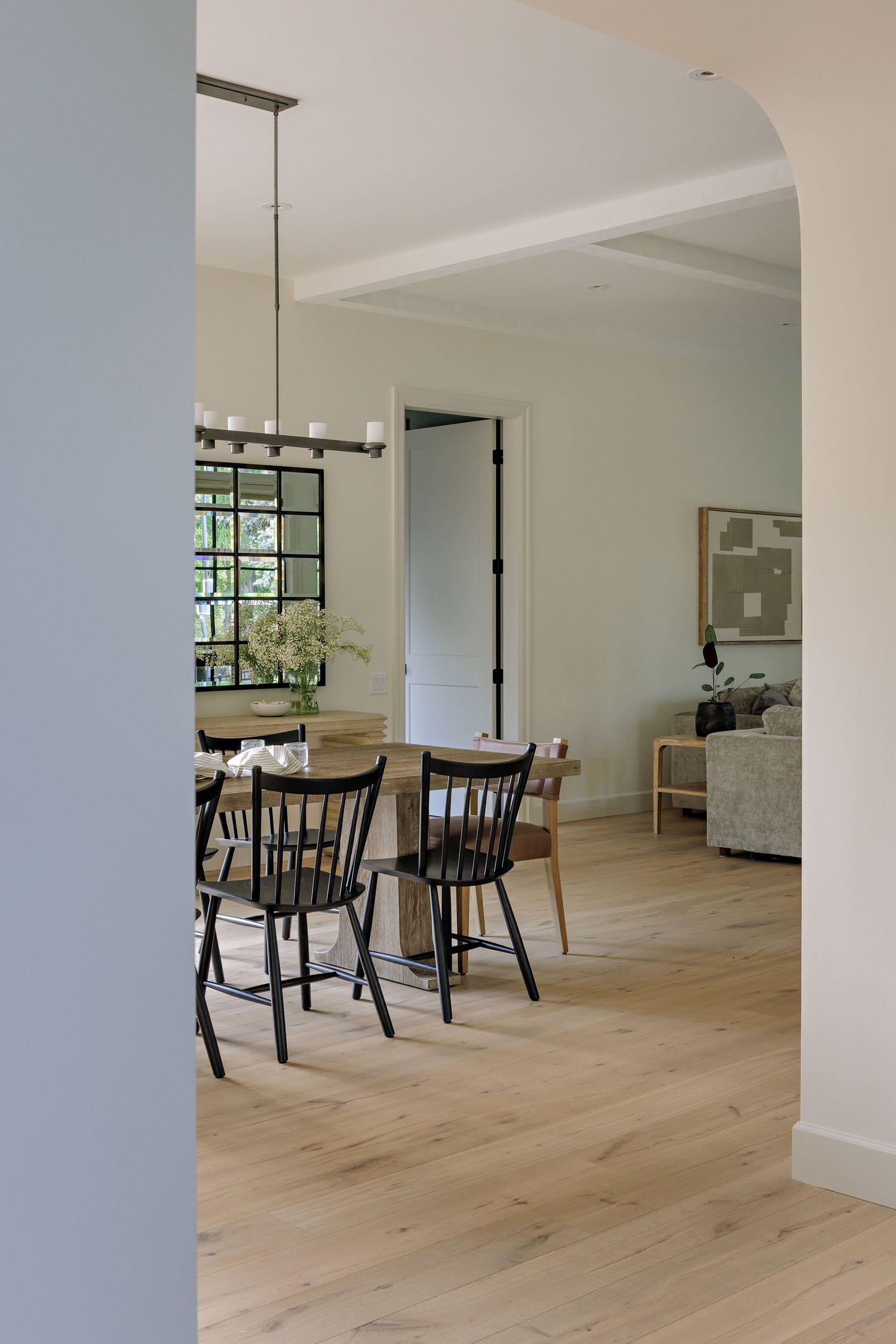 Modern dining area with black Windsor chairs, light wood floors, and large windows in a bright minimalist space.