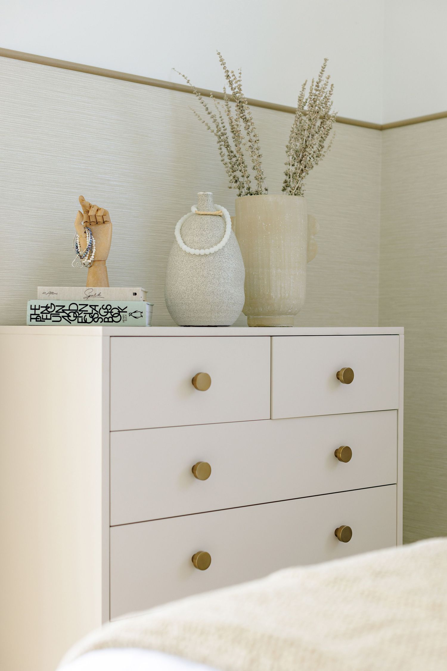 Minimalist white dresser with brass knobs decorated with dried flowers in neutral vases on top.
