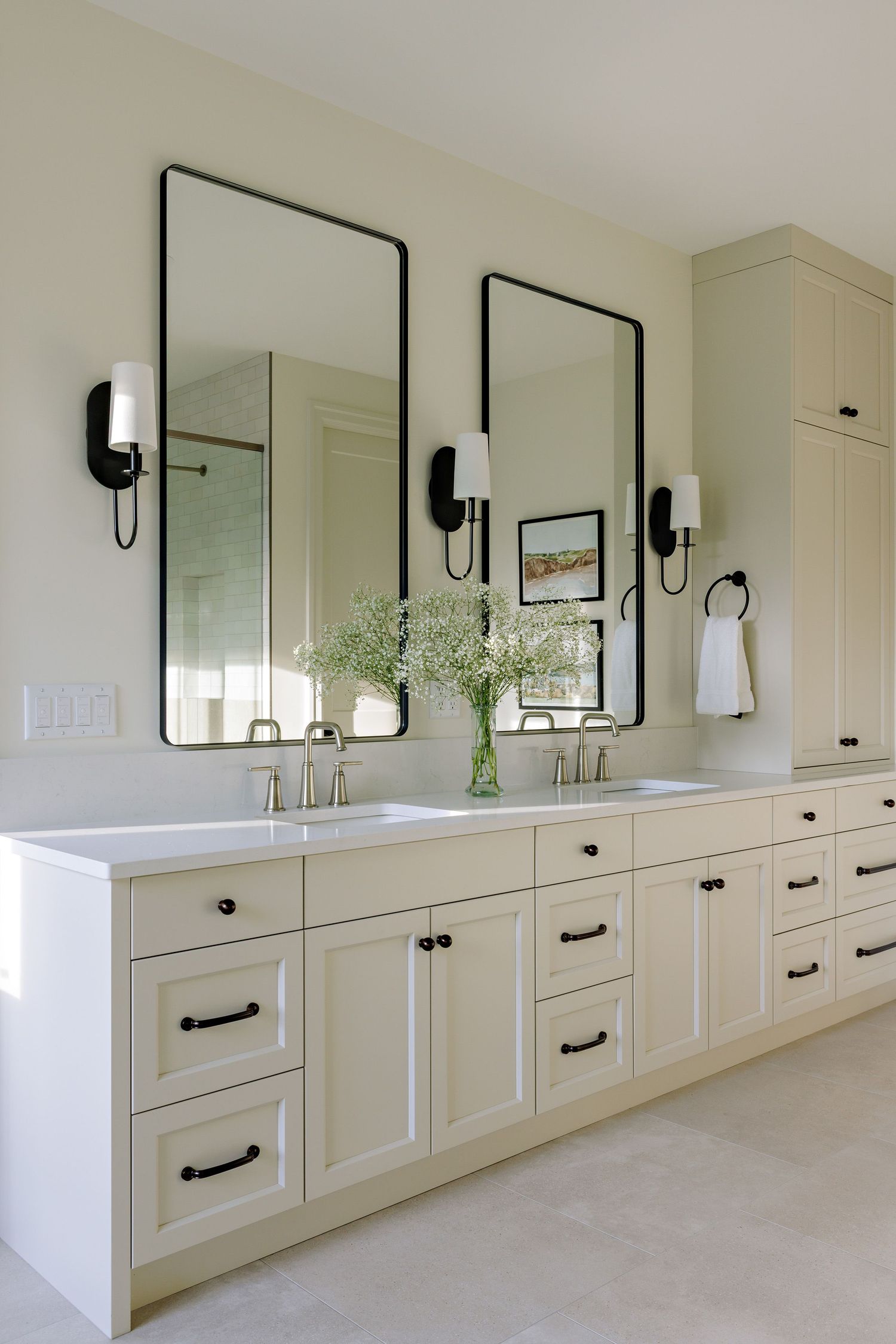 Modern white bathroom vanity with black hardware, rectangular mirrors, and wall sconces creates an elegant aesthetic.