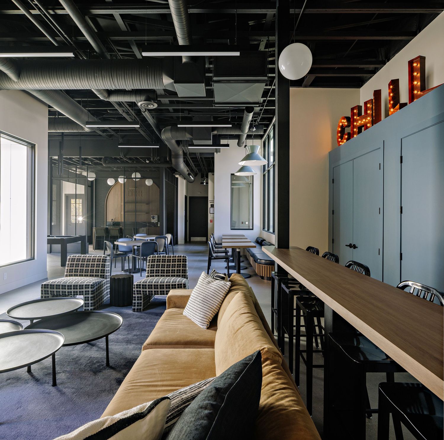 Modern office space with exposed industrial ceiling, sleek furniture, and large windows providing natural light.