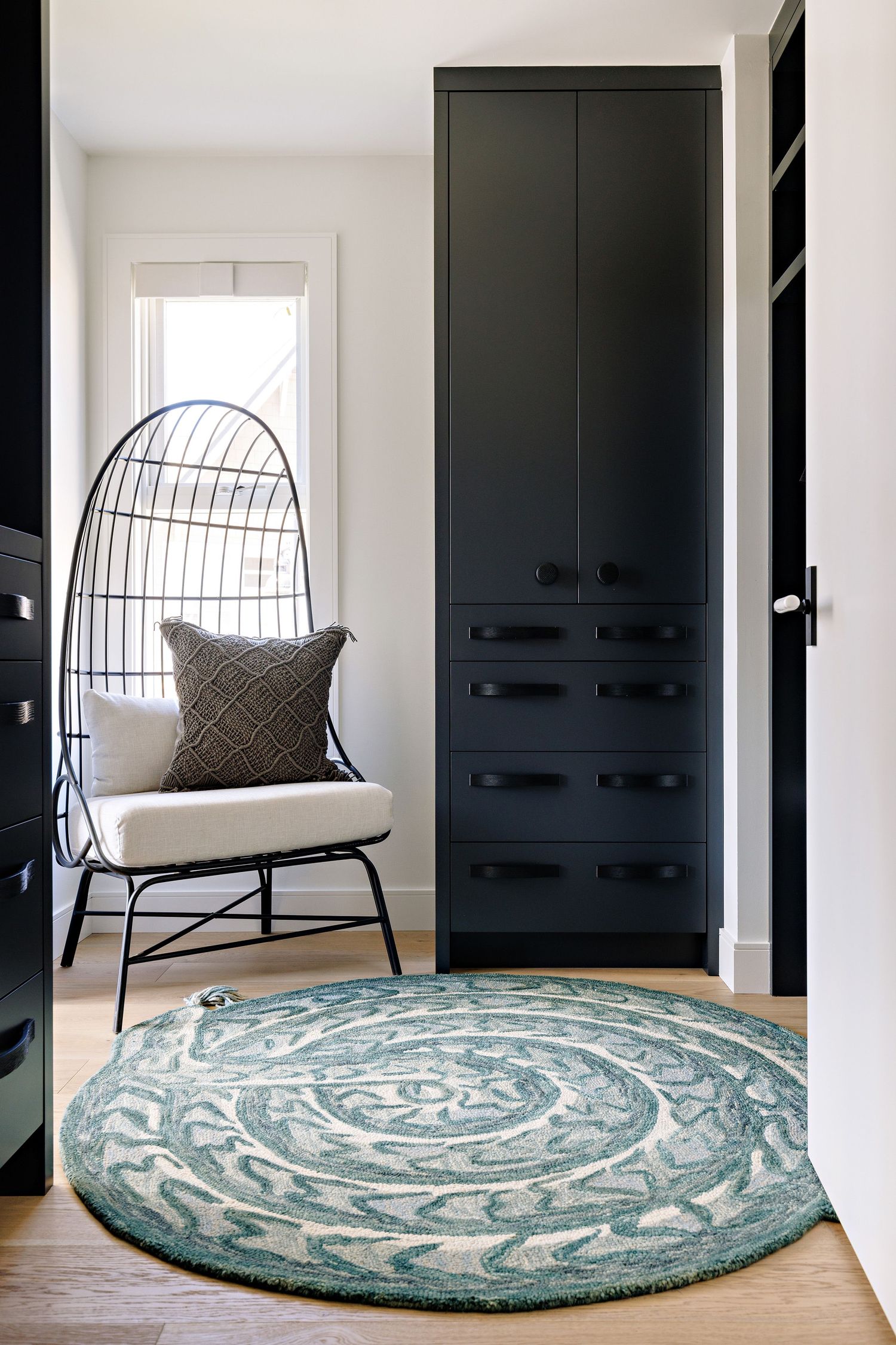 Modern entryway featuring black built-in storage and egg chair with patterned circular rug.