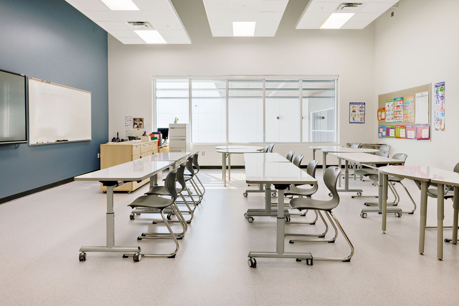 Modern classroom interior with moveable desk tables and ergonomic chairs arranged in rows on white floor.