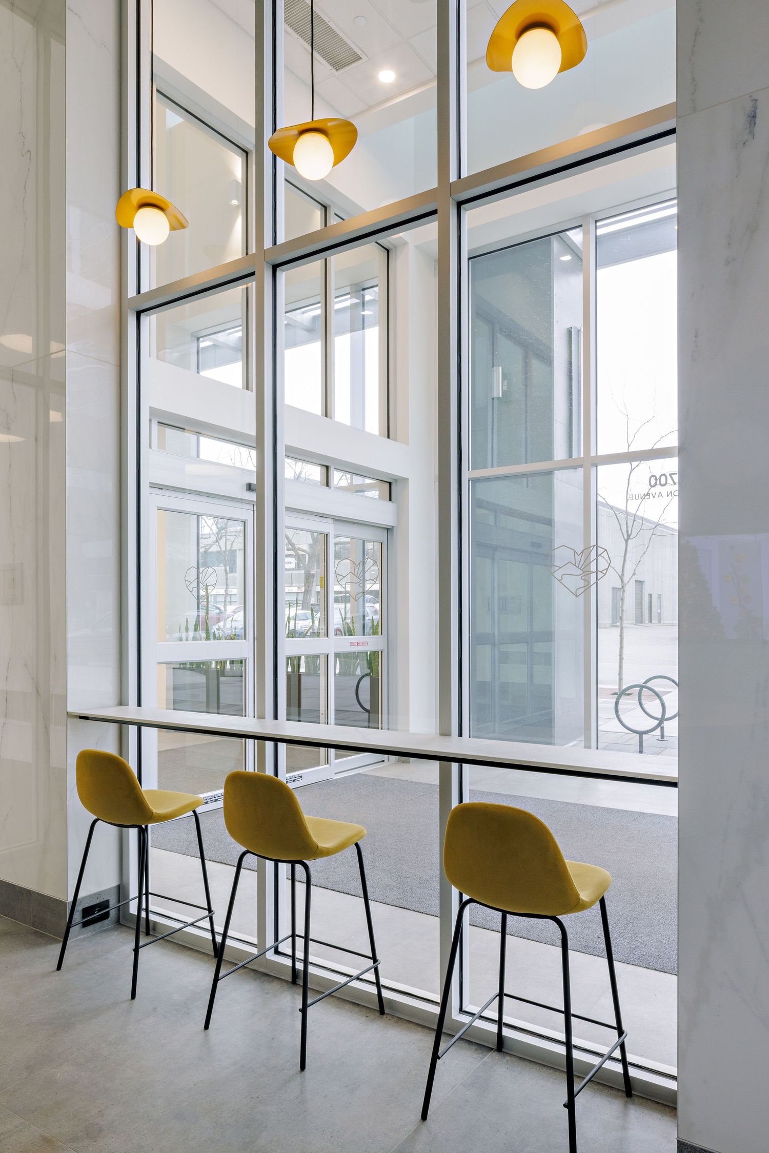 Modern minimalist cafe bar seating with three yellow bar stools against tall windows and pendant lighting.
