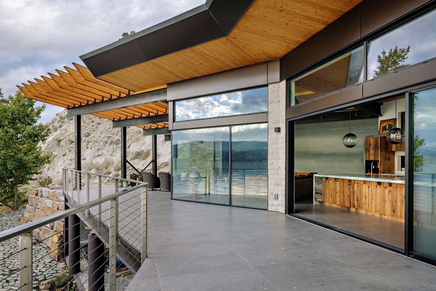 Modern hillside home features expansive glass walls, wood accents, and a sleek horizontal design overlooking a scenic landscape.