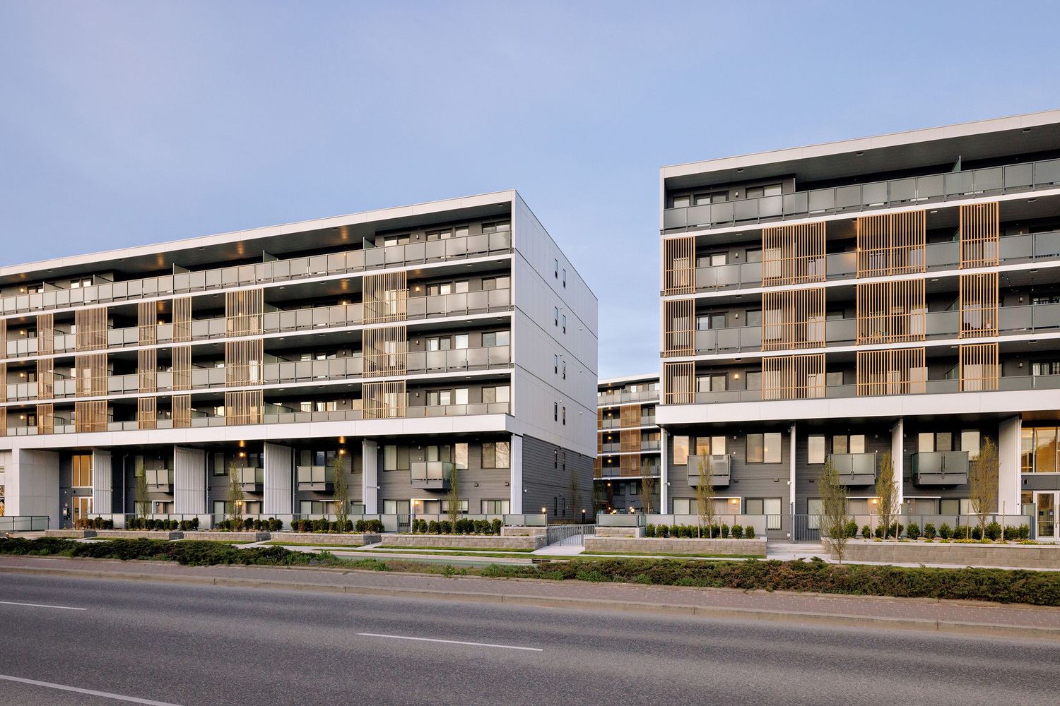 Modern multi-story apartment buildings with balconies and ground floor retail spaces along an urban street.