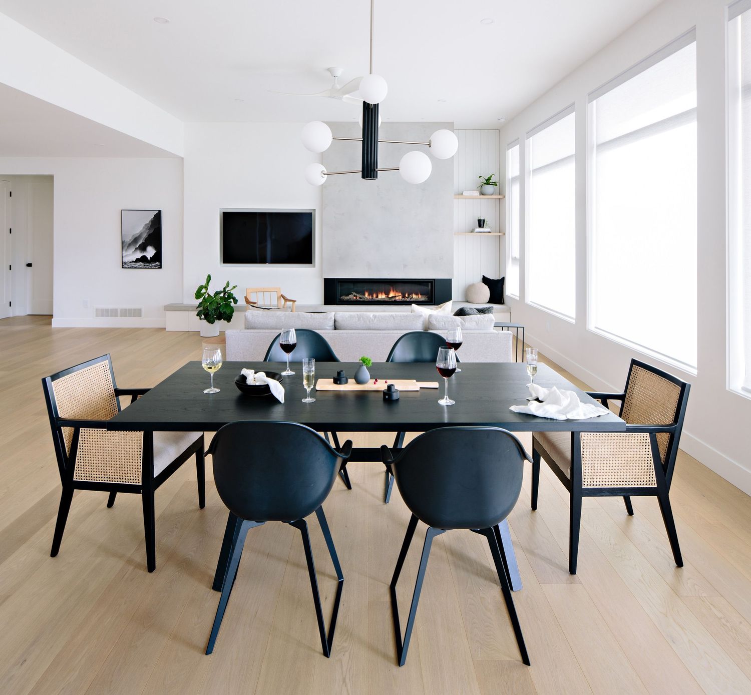 Modern dining area with blue chairs and black table in an open concept living space with linear fireplace.