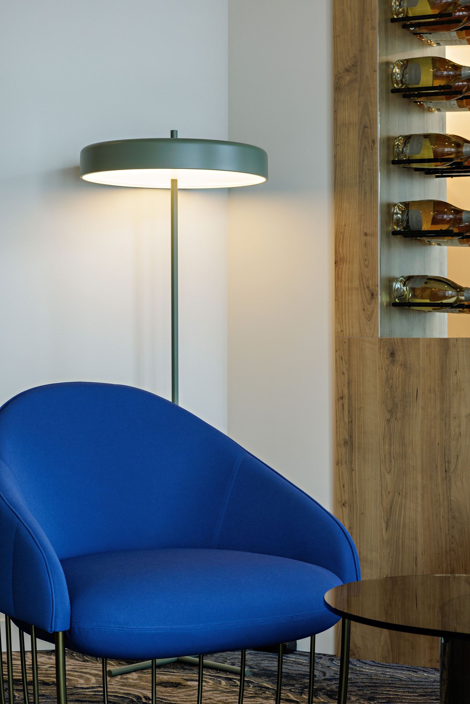 Modern interior featuring a vibrant blue accent chair and sleek floor lamp beside wooden wine storage display.