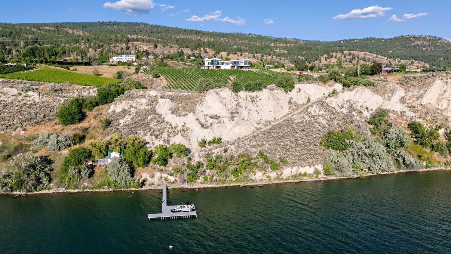 Aerial view of a white sailboat near limestone cliffs along a lake surrounded by green landscape.