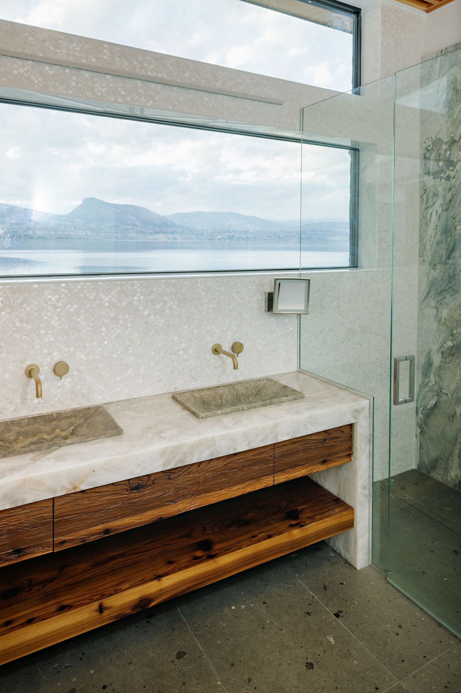 Modern bathroom vanity with wooden base and marble countertop featuring panoramic mountain views through horizontal windows.