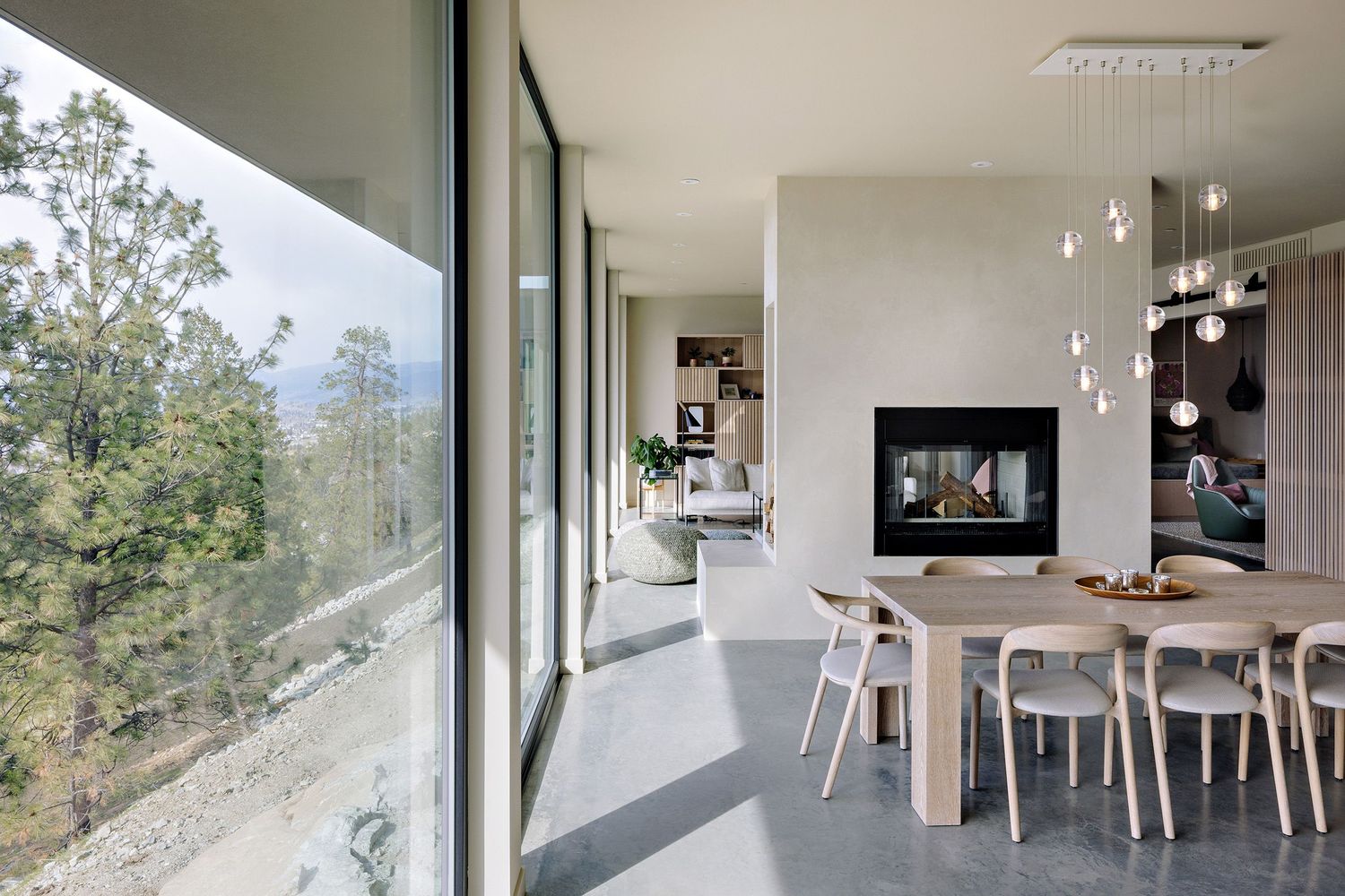 Modern open-concept dining area with floor-to-ceiling windows, sleek fireplace, and pendant lights overlooking scenic mountain views.