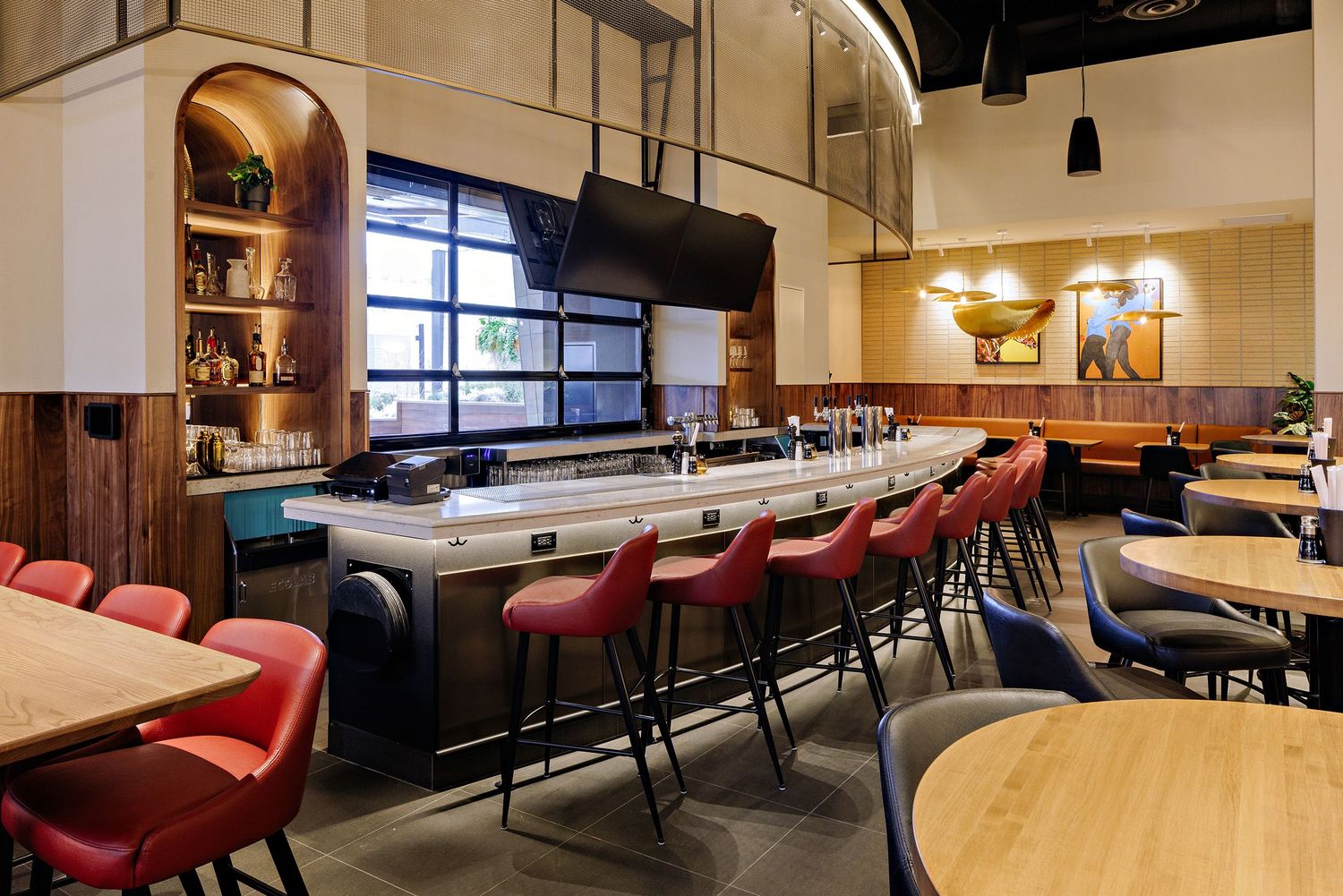 Modern restaurant interior with curved bar counter, red leather barstools, and warm lighting against wooden accents.
