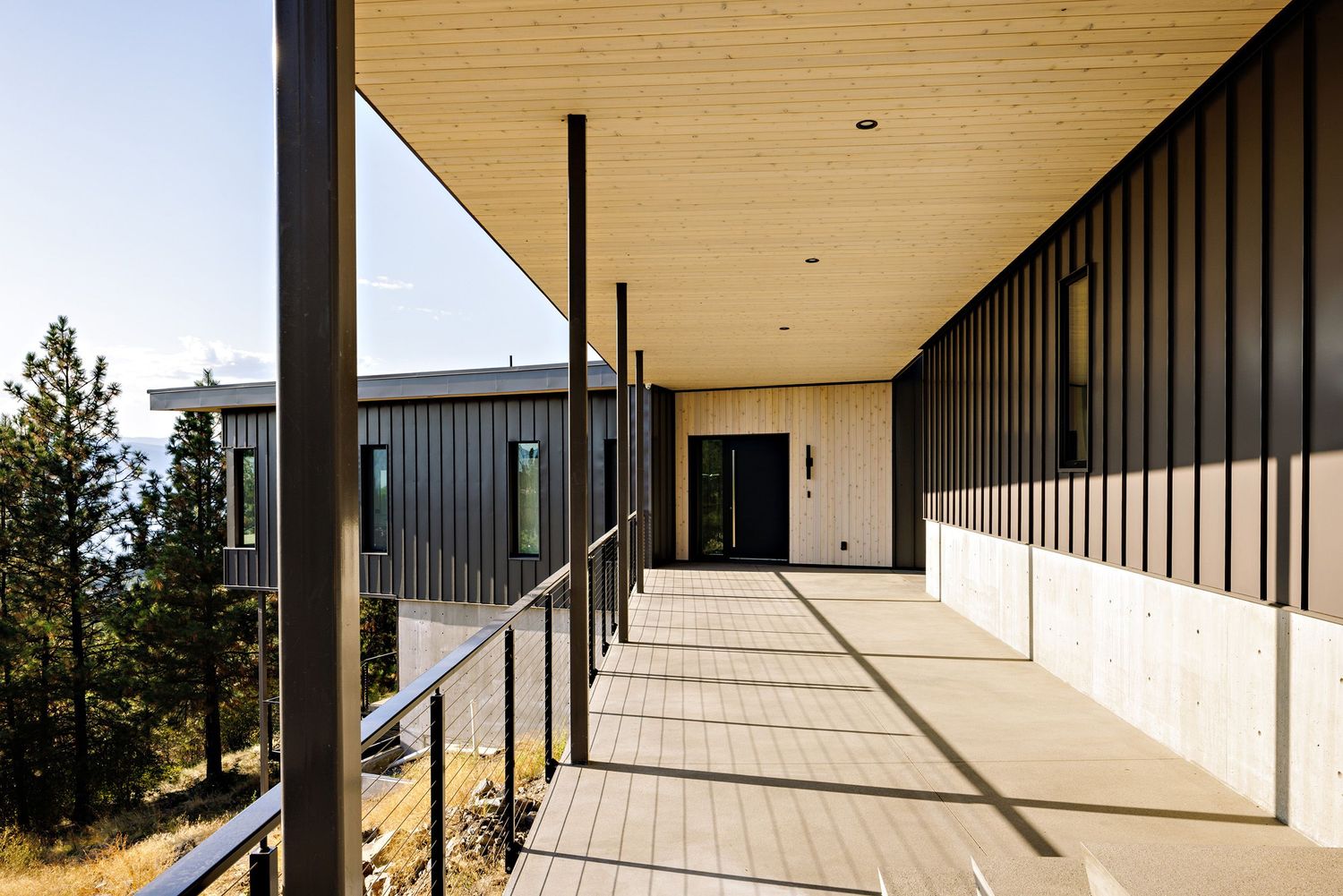 Modern building exterior with covered walkway featuring clean lines, black vertical slats, and warm wood ceiling details.