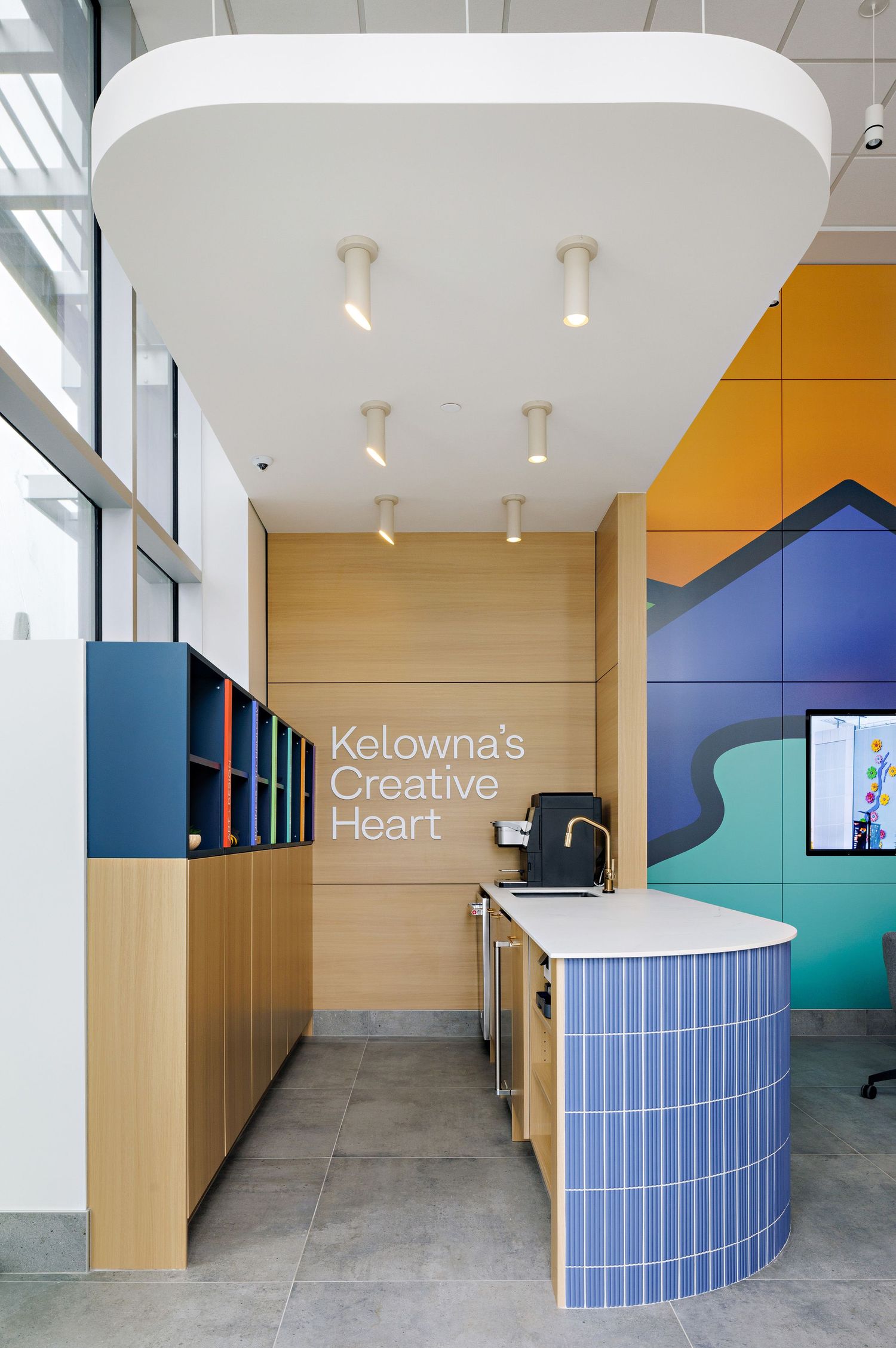 Modern office reception area with curved tiled counter, wooden cabinets, and signage reading 'Kelowna's Creative Heart' on wall.