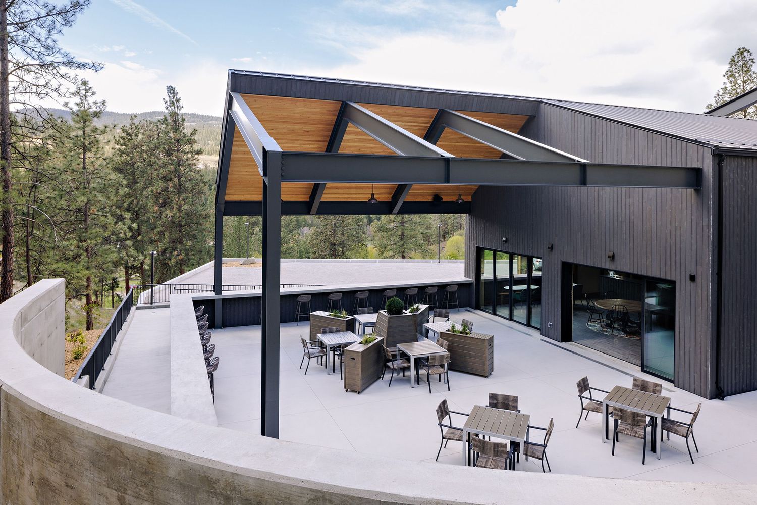 Modern outdoor patio with angular roof design features multiple seating areas surrounded by mountain views and pine trees.