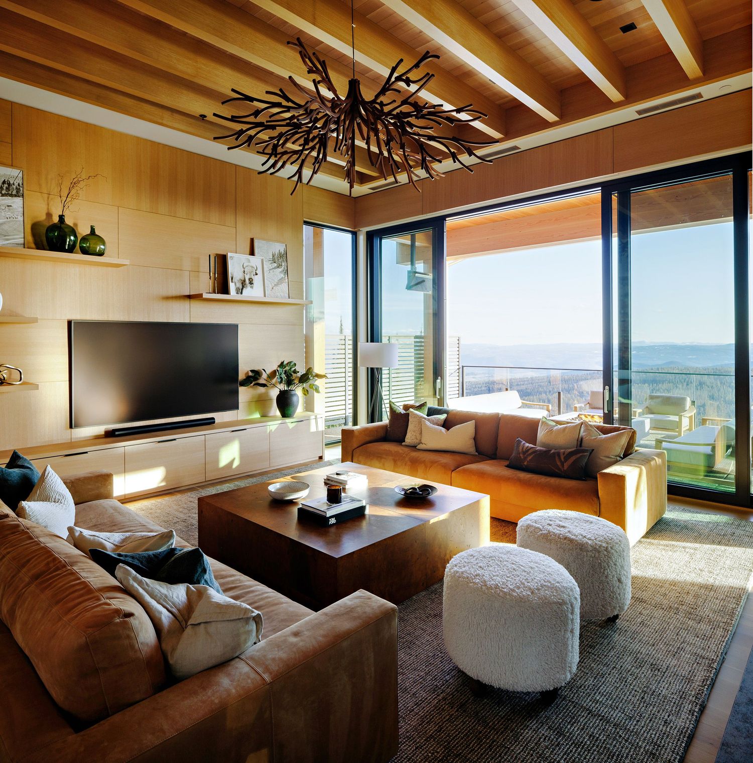 Modern living room with panoramic views featuring wood ceilings, brown leather sofa, and unique black chandelier.