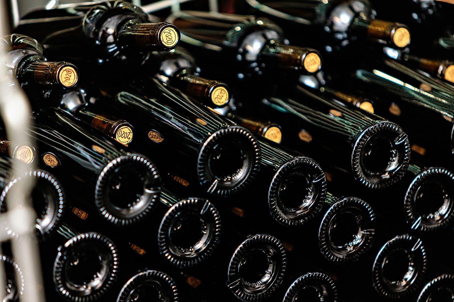 Rows of dark glass wine bottles with gold capsules stacked horizontally in wine cellar storage.