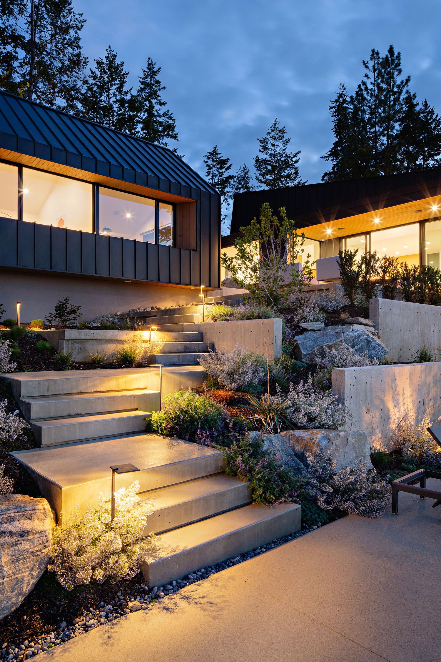 Modern hillside home with illuminated outdoor stairs and landscaping at twilight featuring warm lighting and contemporary design.