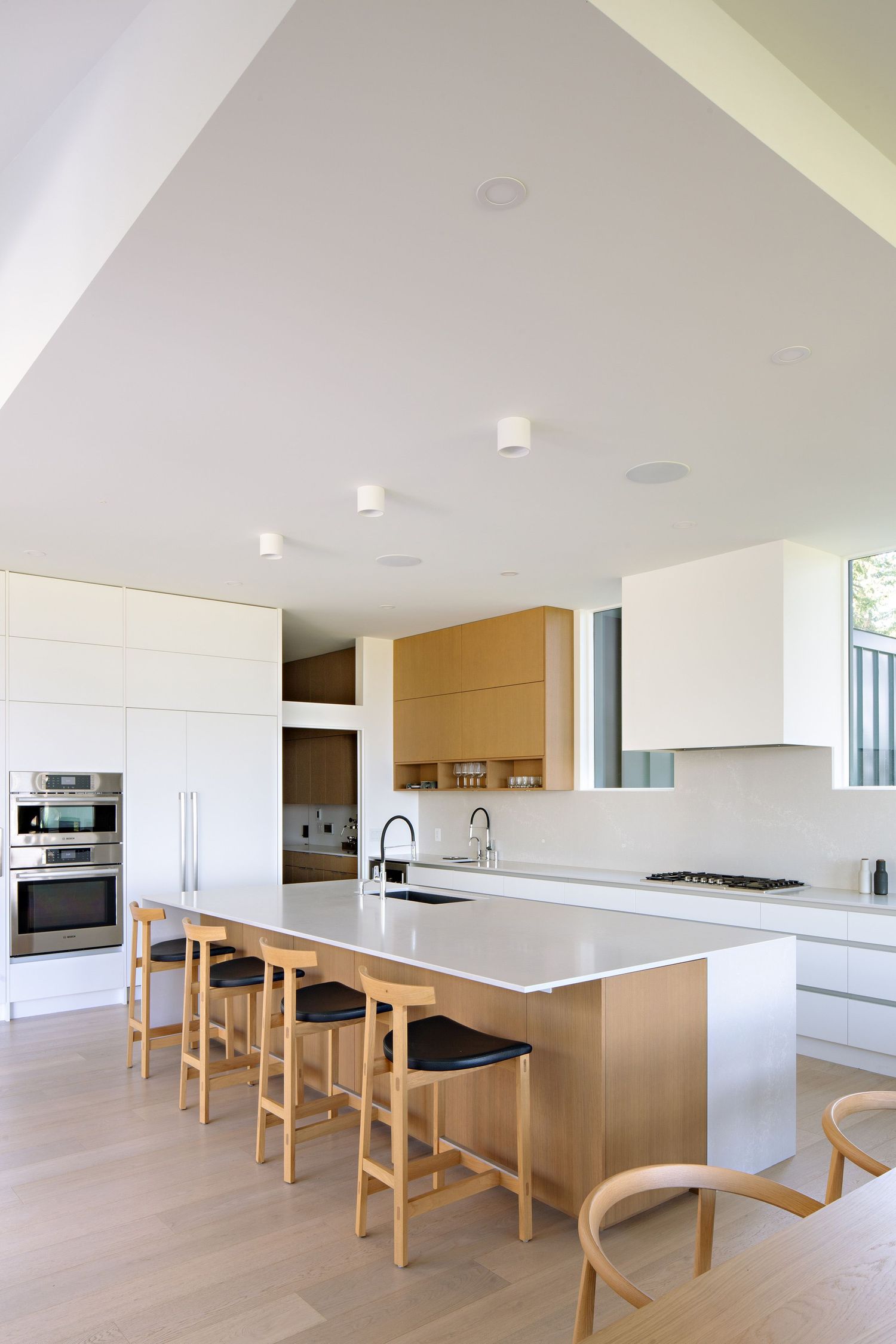 Modern white and gold kitchen with waterfall island counter, wooden bar stools, and sleek built-in appliances.