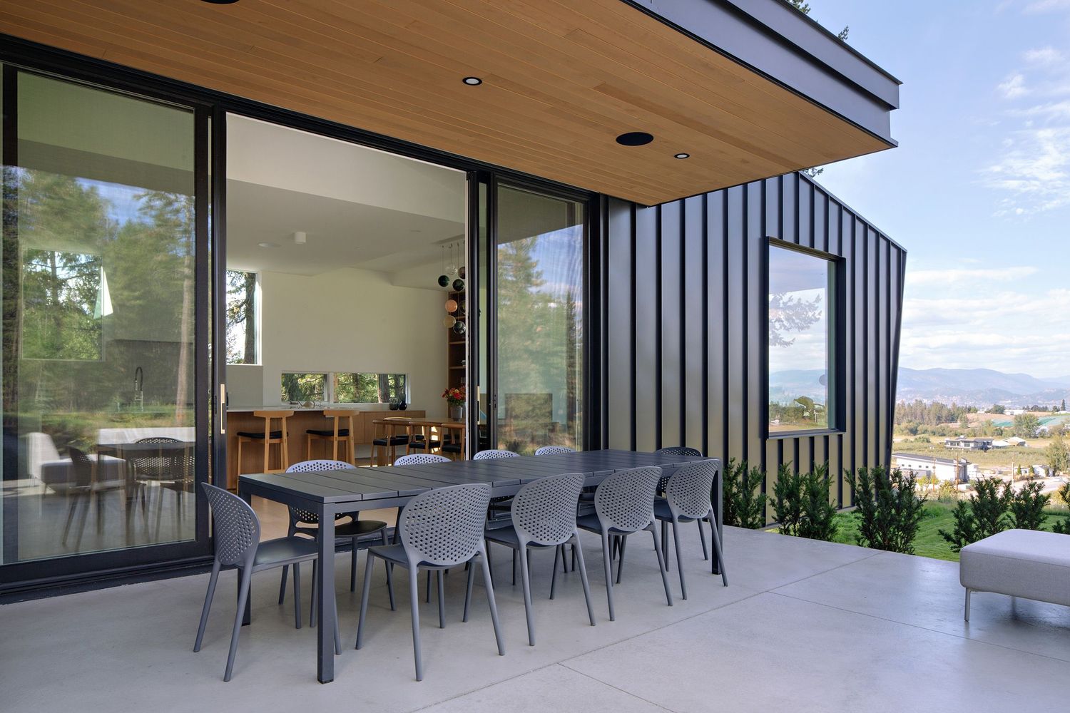Modern outdoor patio area with gray chairs and glass walls overlooking a scenic city view.