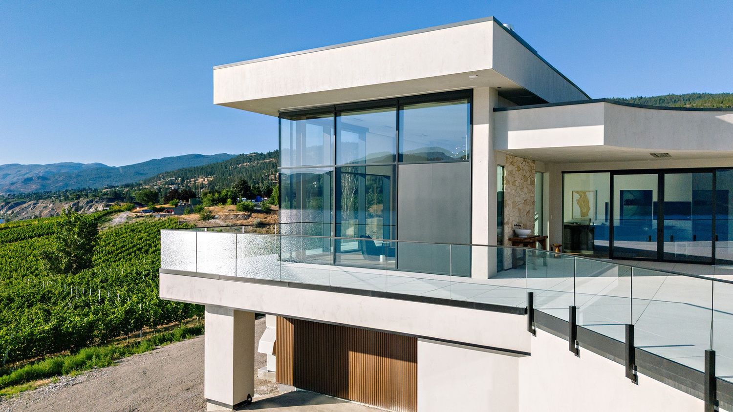 Modern luxury villa with panoramic glass walls and infinity pool overlooking a lush mountain landscape at sunset.