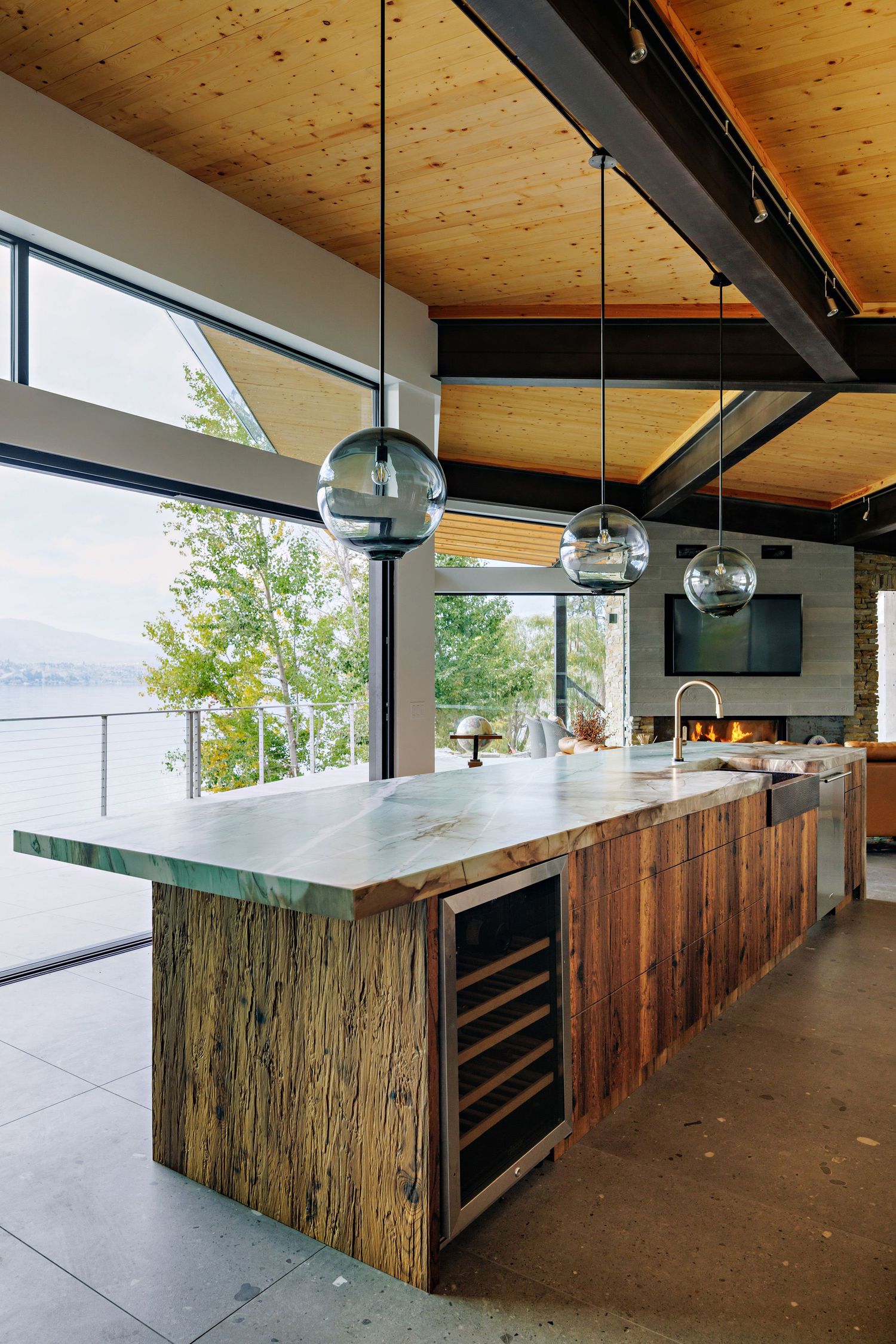 Modern kitchen island features reclaimed wood paneling and sleek white countertop under wooden ceiling with black beams.