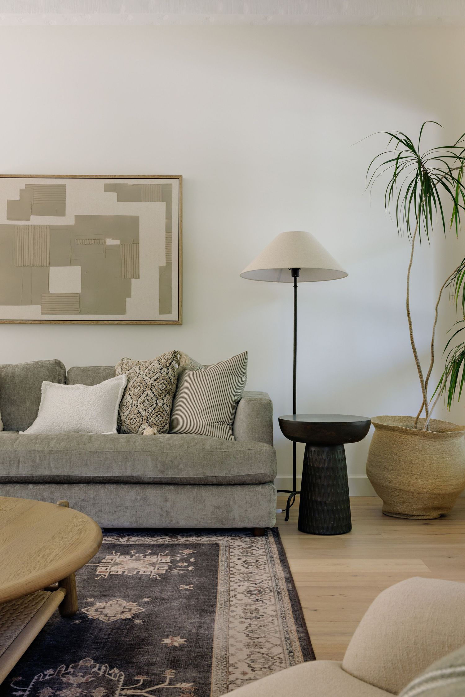 Modern living room with gray sofa, abstract wall art, floor lamp, and potted palm plant in minimalist neutral decor.