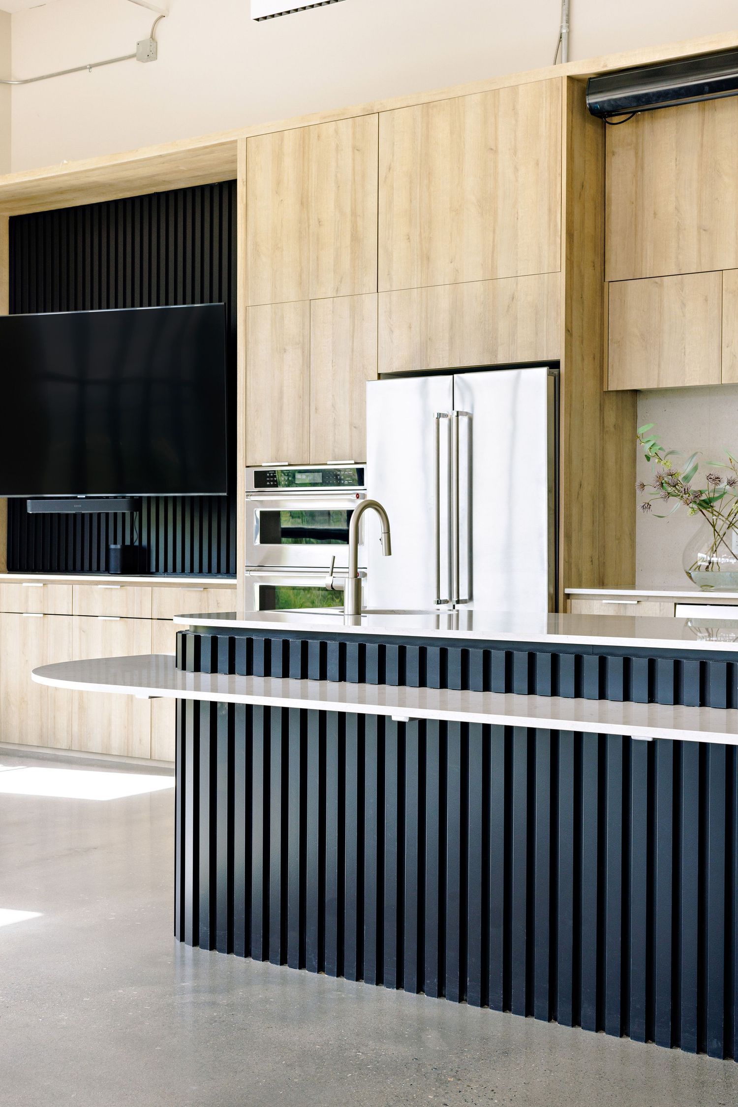 Modern kitchen design with light wood cabinets and black ribbed island featuring stainless steel appliances and minimalist decor.