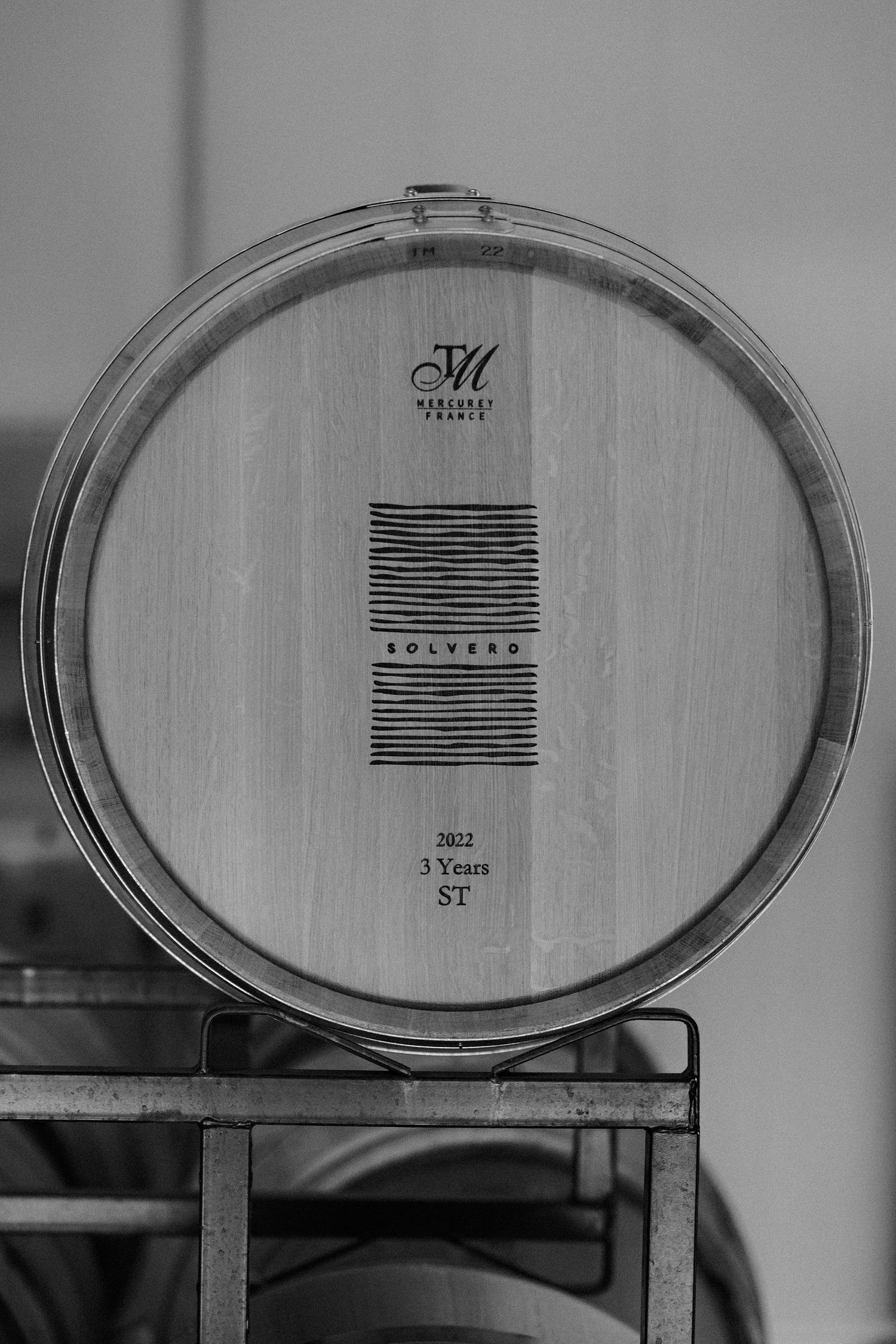 A black and white photograph of a large wooden wine barrel with geometric markings on its surface.