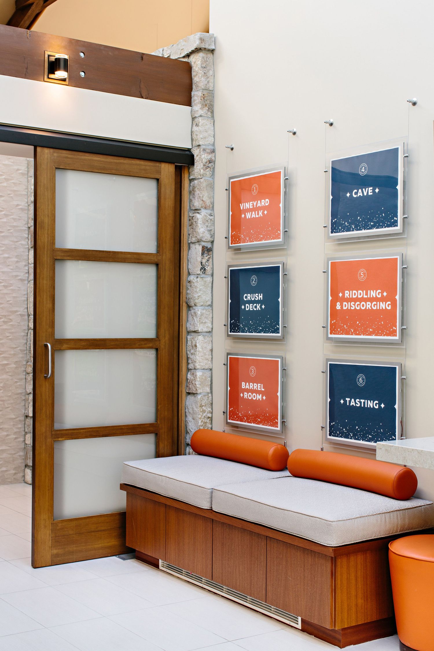 Modern tasting room interior with orange and blue framed menu signs and wooden bench seating.