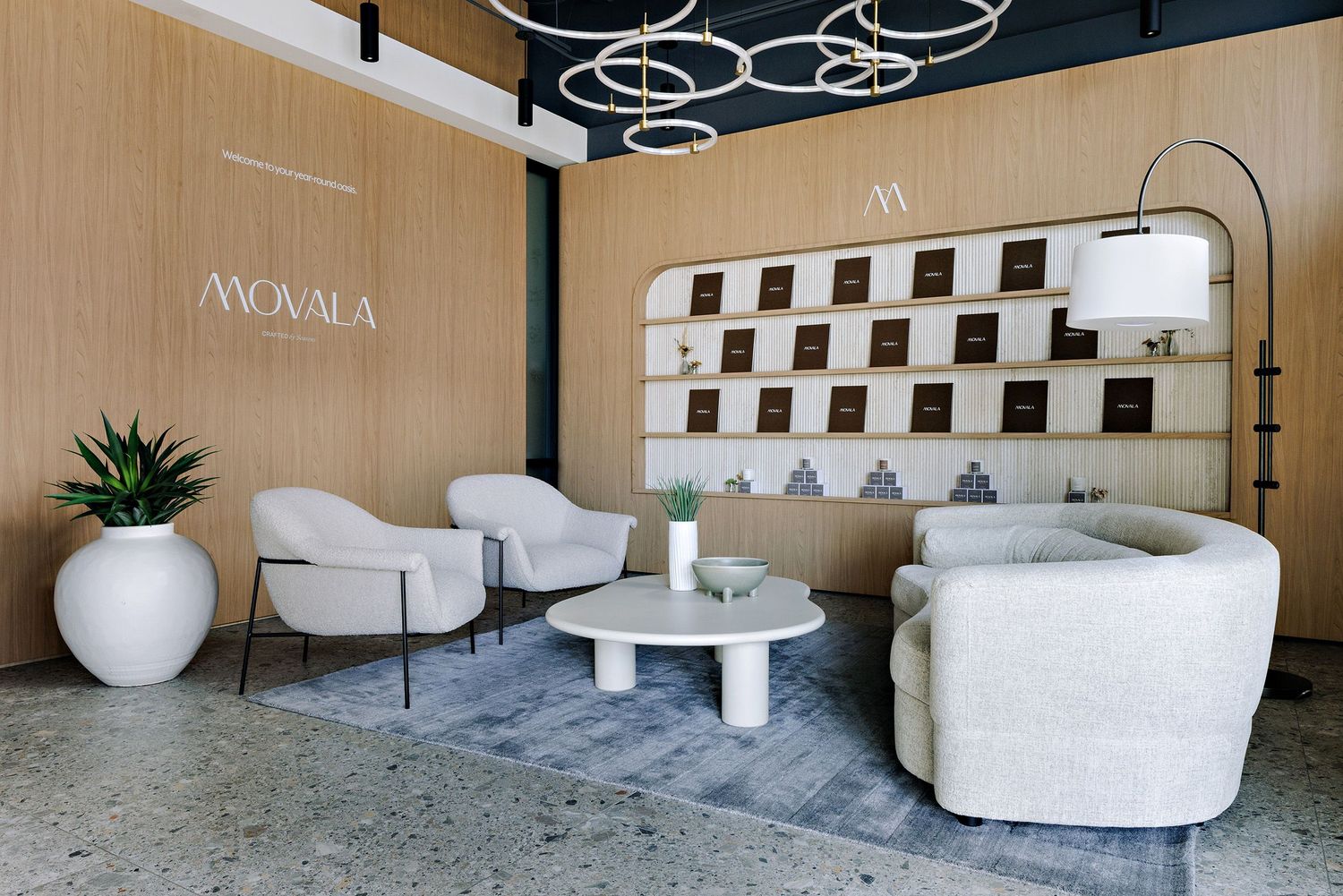 Modern waiting area with curved white chairs, decorative ceiling lights, and a modular wall display in a sleek office space.