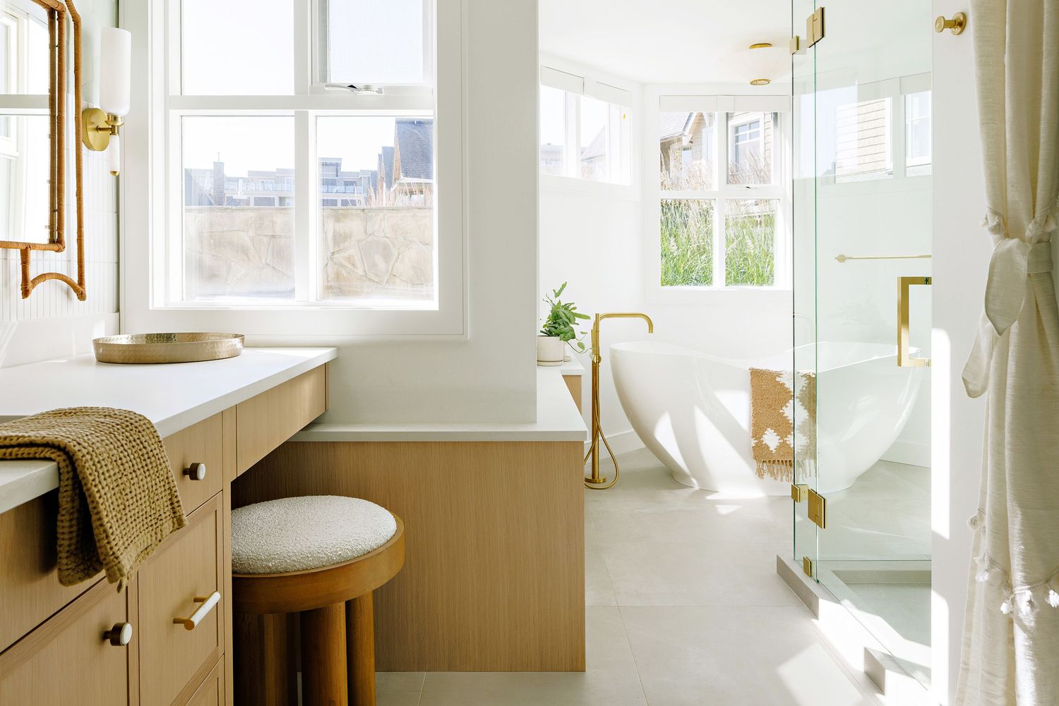 Bright modern bathroom with white walls, wooden vanity, and brass fixtures overlooking city views.