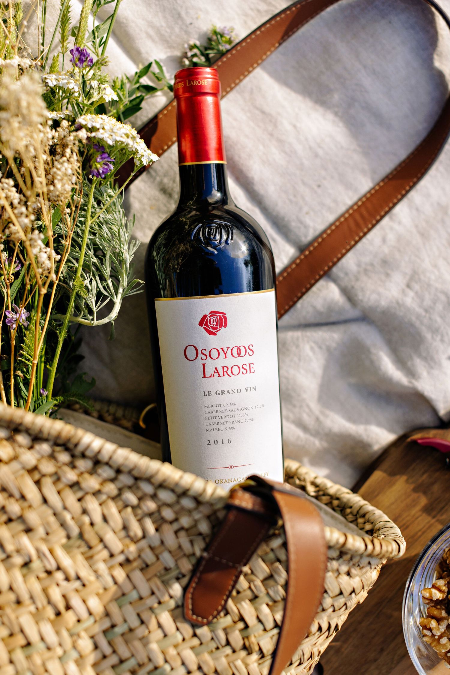 Bottle of Osoyoos Larose wine displayed with wildflowers in woven picnic basket.