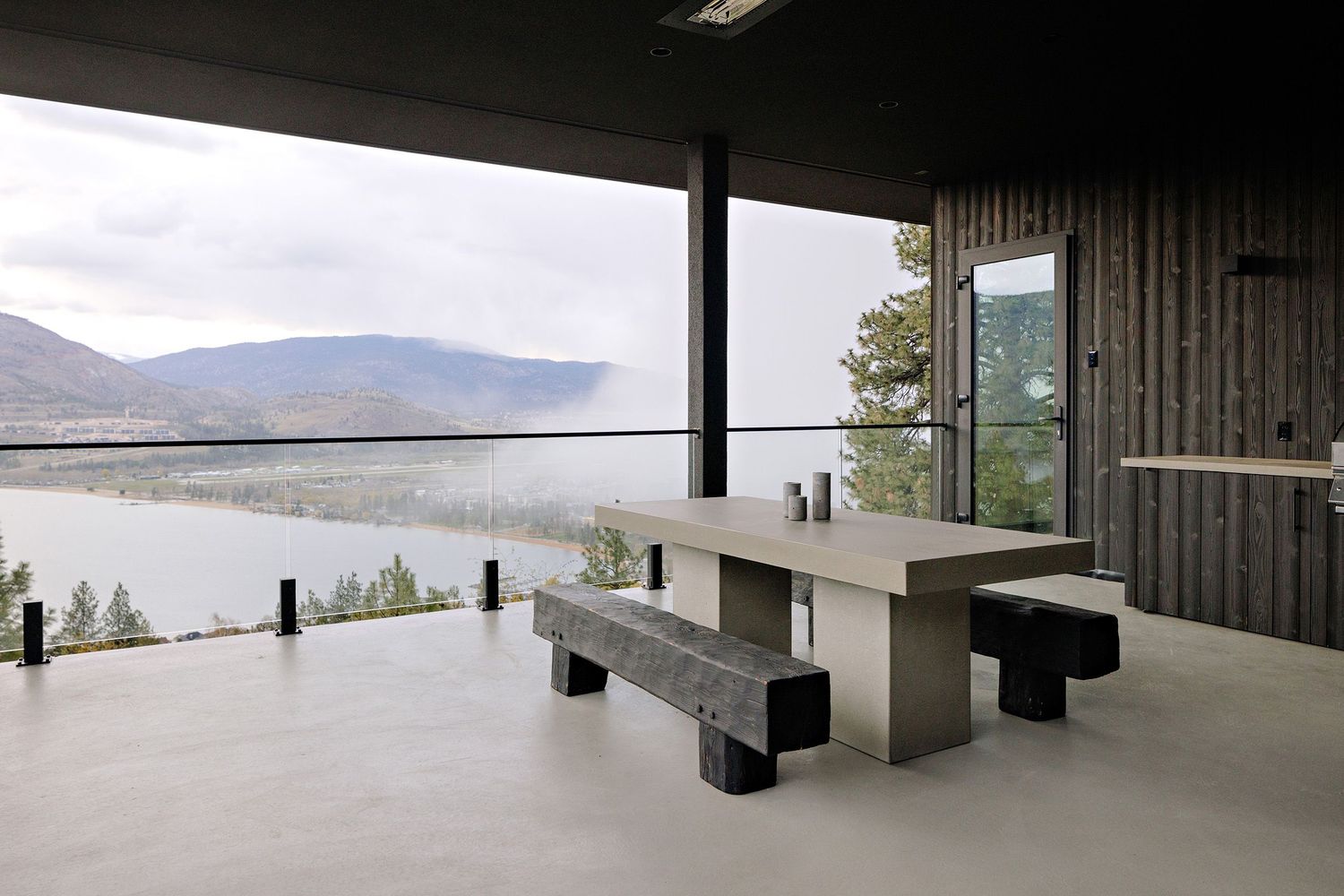 Outdoor dining area with a concrete table and benches overlooking a serene mountain lake landscape.
