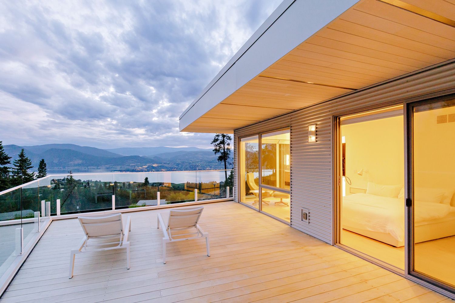 Modern hillside home with large deck and sliding glass doors showcases stunning mountain views at dusk.
