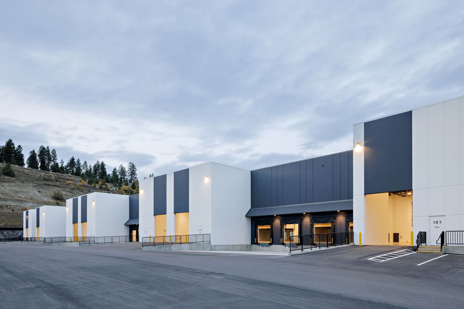 Modern industrial warehouse facility with white and gray exterior features illuminated loading docks at dusk.