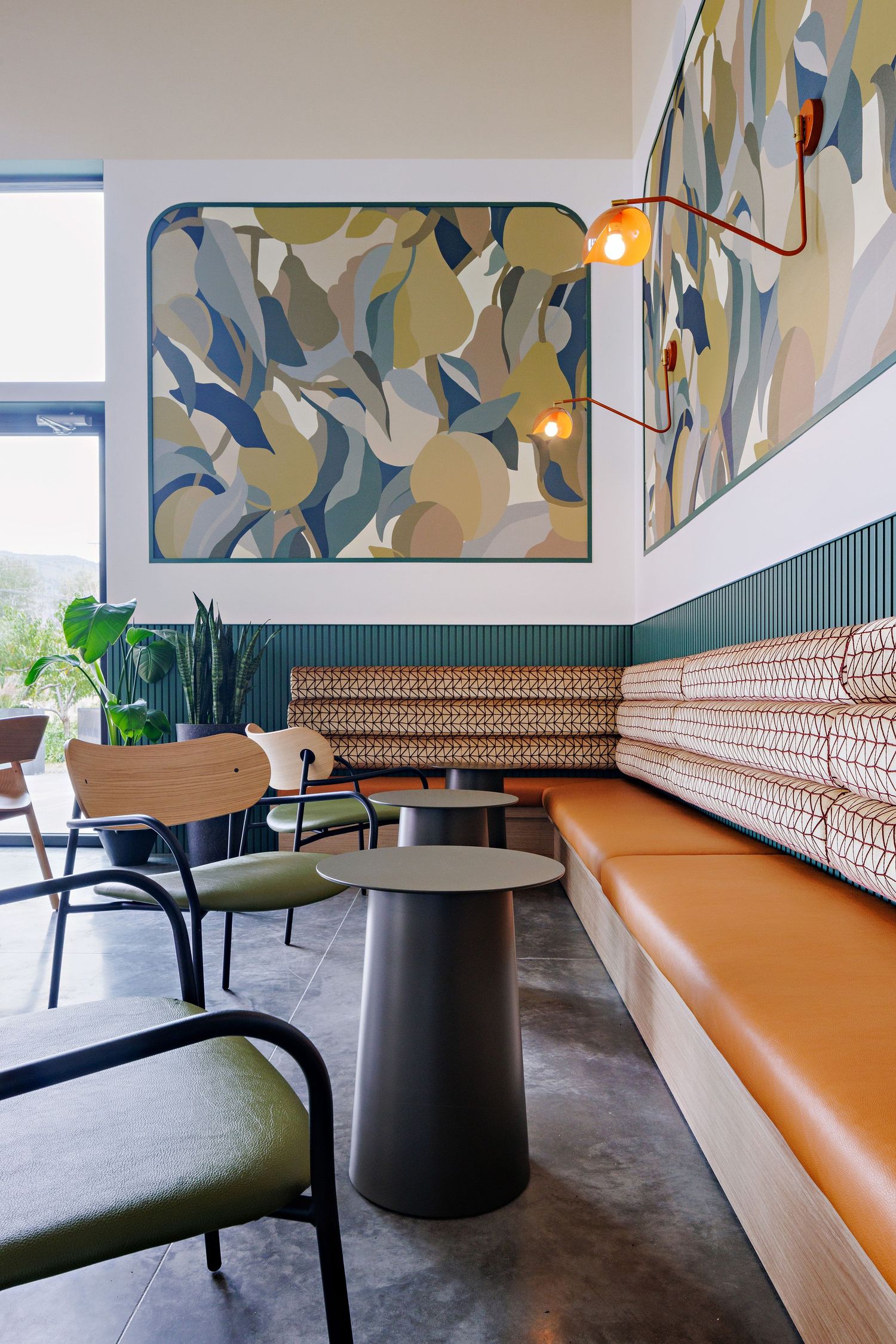 Modern cafe interior with abstract wall art, orange banquette seating, and green wainscoting against white walls.