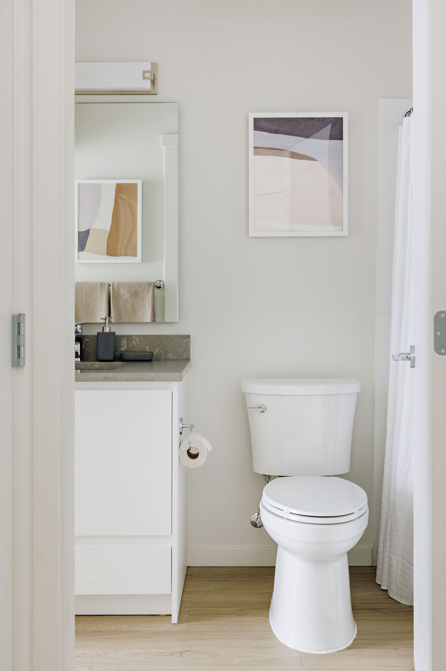 Modern minimalist bathroom interior with white toilet, mirror, and abstract art on light walls.