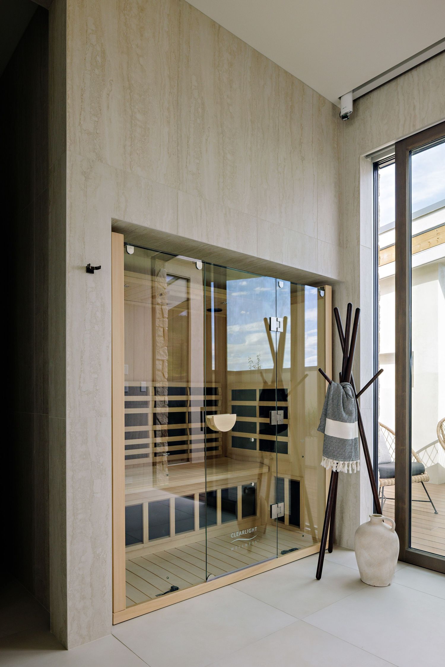 Modern home spa featuring a glass-enclosed sauna with wooden interior and decorative vases beside large windows.