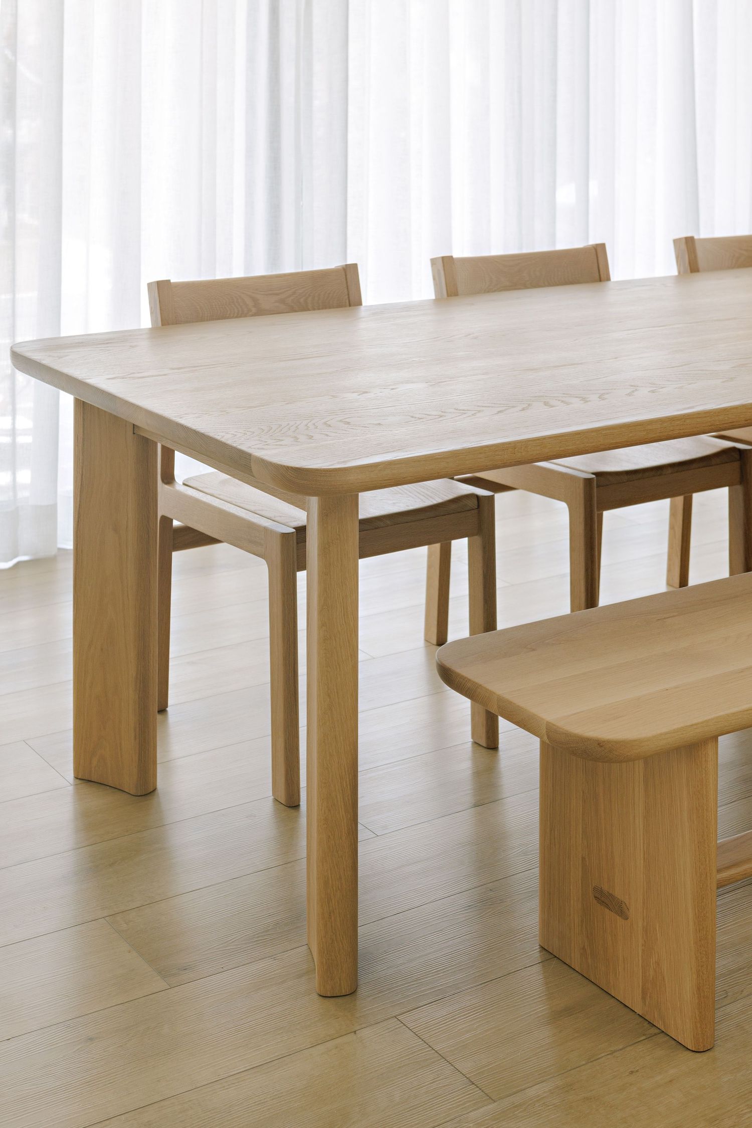 Modern minimalist wooden dining table and bench set with clean lines and natural finish in bright interior space.