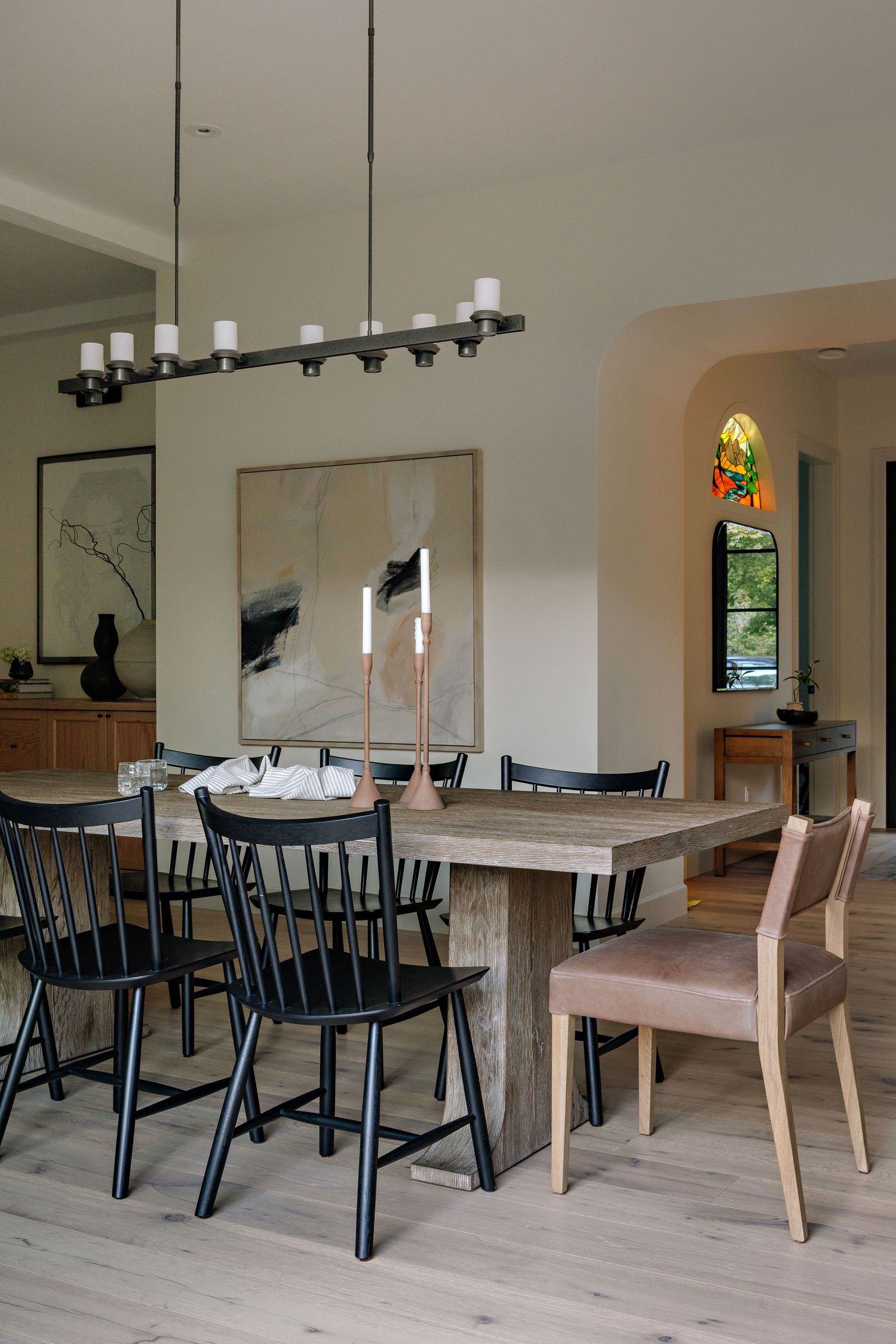 Modern dining room with rustic wooden tables and black Windsor chairs arranged in rows beneath pendant lighting.