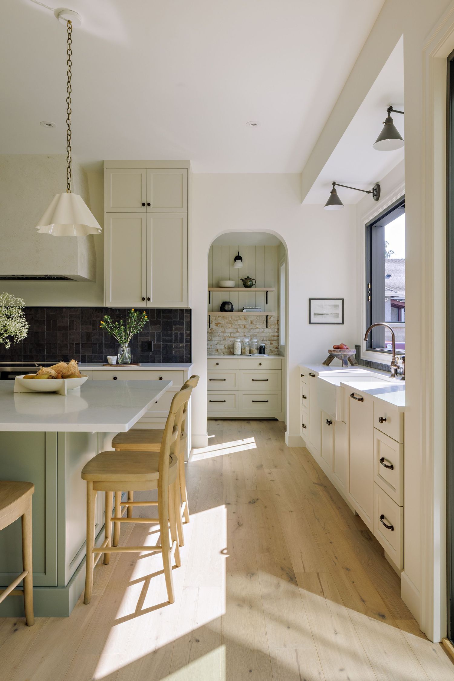 Modern kitchen interior with light wood floors, white cabinets, and sage green accents shown from multiple angles in natural light.
