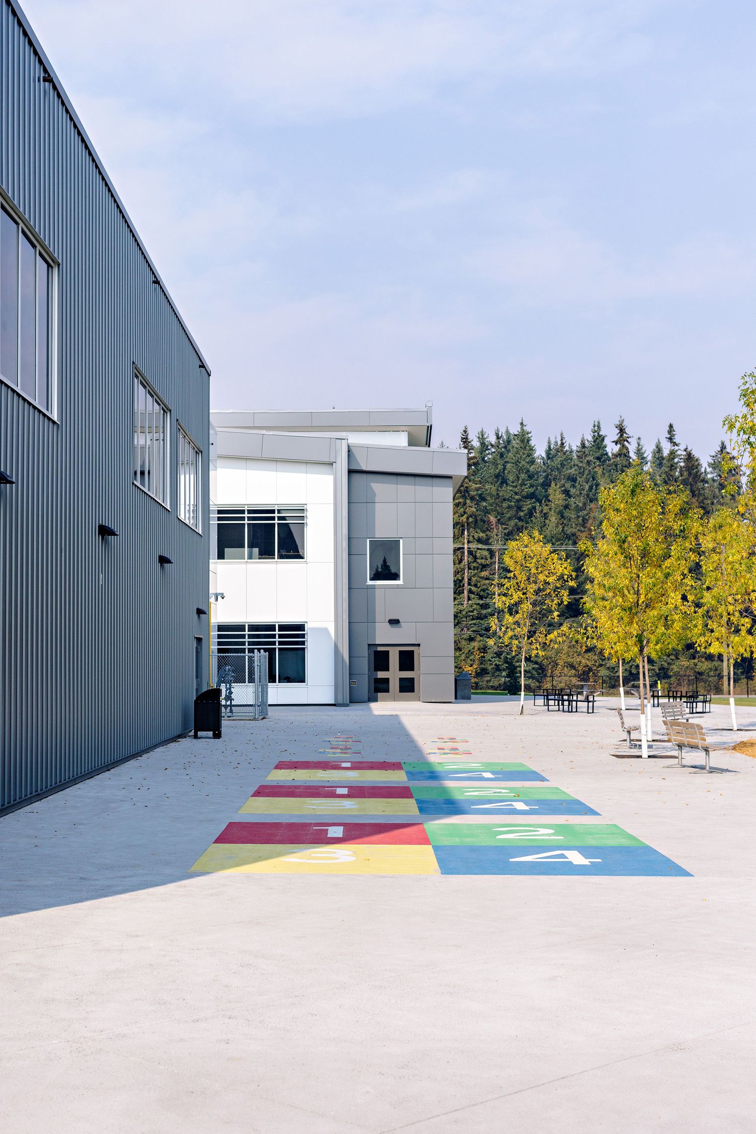 Modern school building exterior with colorful hopscotch pattern painted on concrete and yellow autumn trees in background.