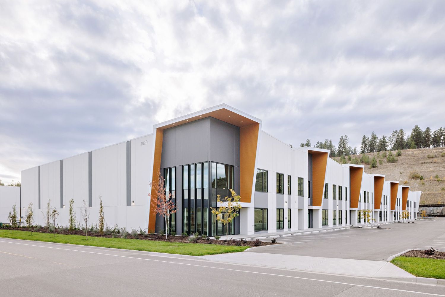 Modern industrial business park with white buildings featuring orange accent panels and large glass windows.